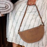Person wearing a patterned dress and brown boots, holding a brown handbag.