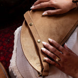 Person holding a brown leather clutch bag with a blurred indoor background