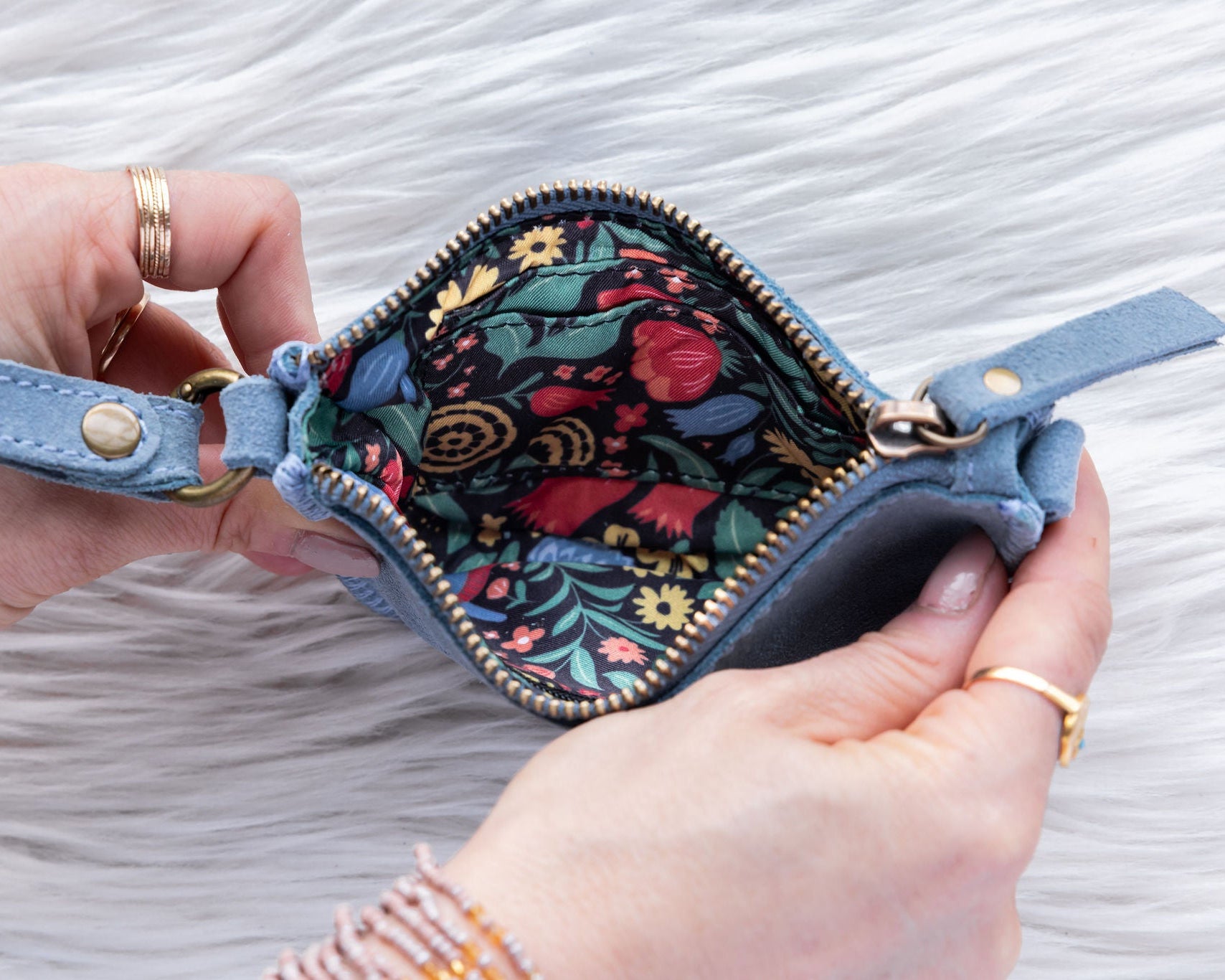Hand holding a blue floral-patterned wallet against a textured white background