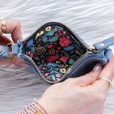 Hand holding a blue floral-patterned wallet against a textured white background