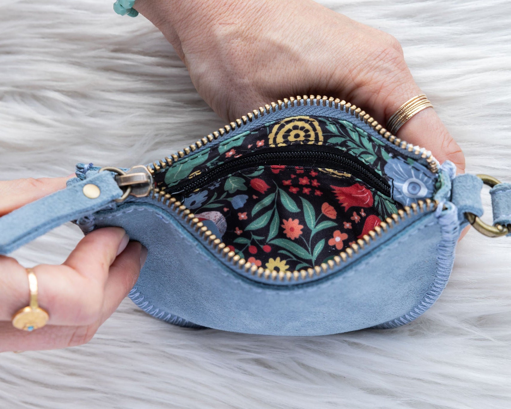 Blue denim pouch with floral interior held by a hand on a gray background