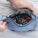 Blue denim pouch with floral interior held by a hand on a gray background