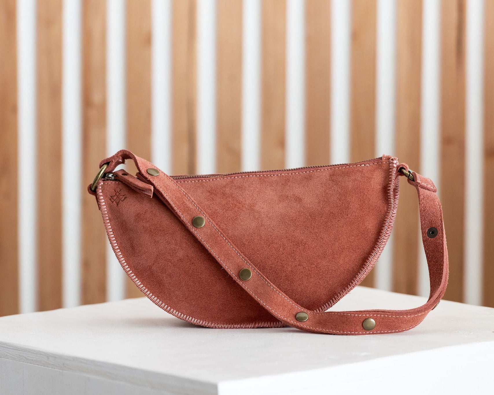 Mauve leather handbag with gold studs on a white surface with a wooden background