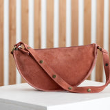 Mauve leather handbag with gold studs on a white surface with a wooden background
