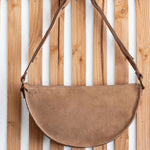 Brown suede handbag with leather strap hanging on a wooden slatted wall.
