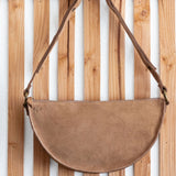 Brown suede handbag with leather strap hanging on a wooden slatted wall.