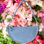 Blue handbag held by a hand against a colorful floral background