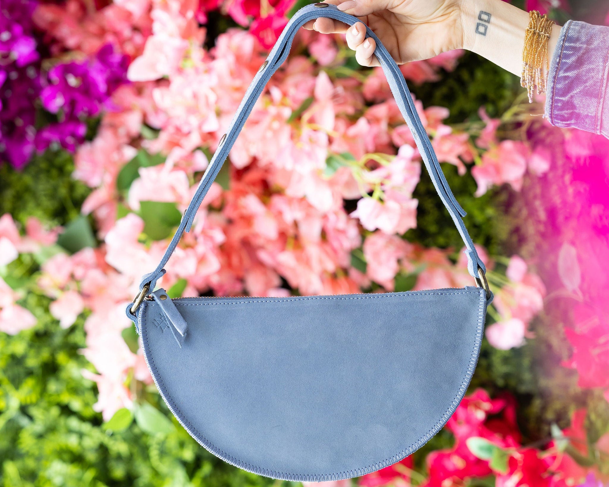Blue handbag held by a hand against a colorful floral background