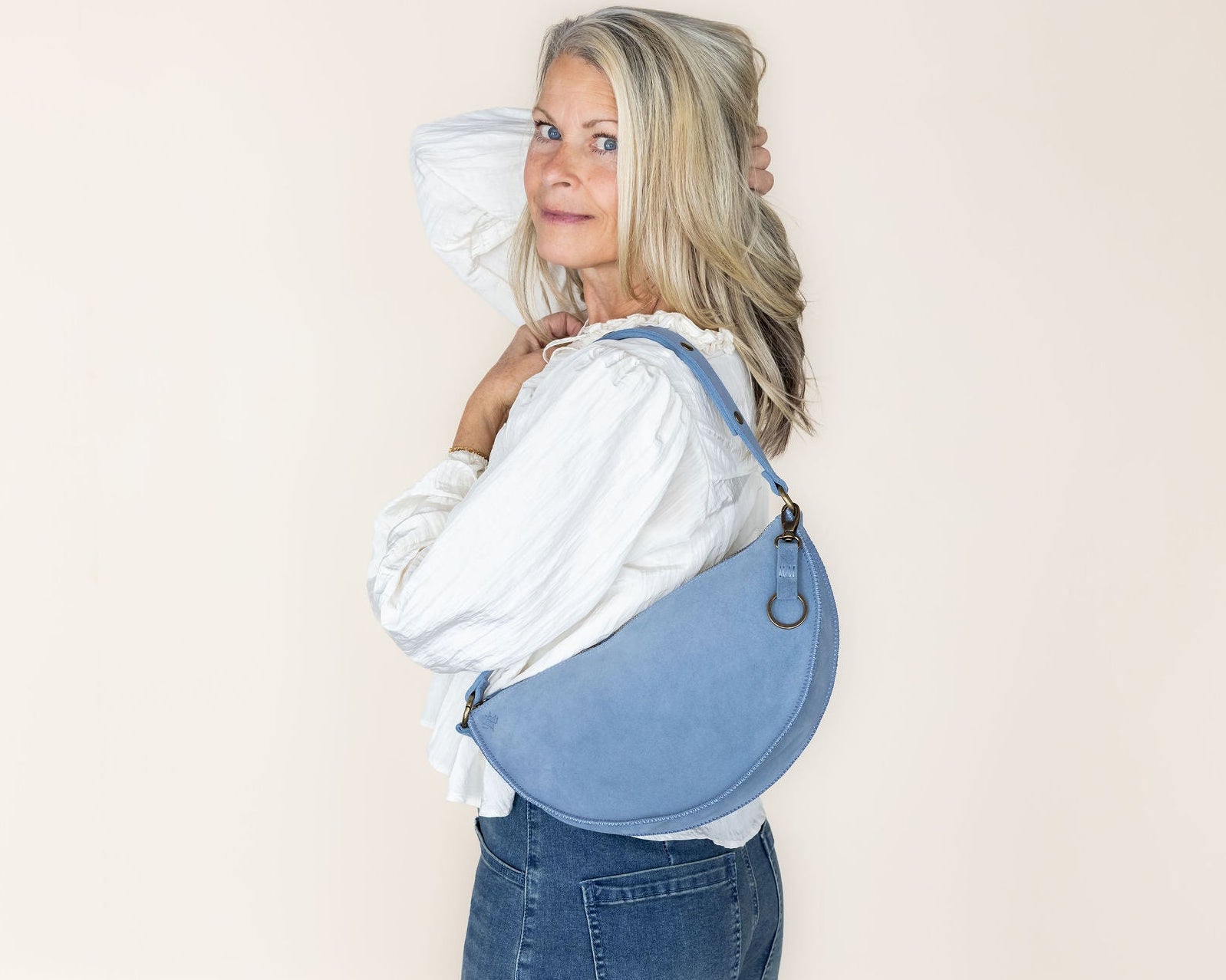 Woman wearing a blue denim bag over her shoulder against a plain background
