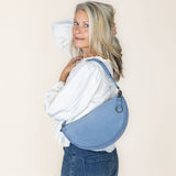 Woman wearing a blue denim bag over her shoulder against a plain background