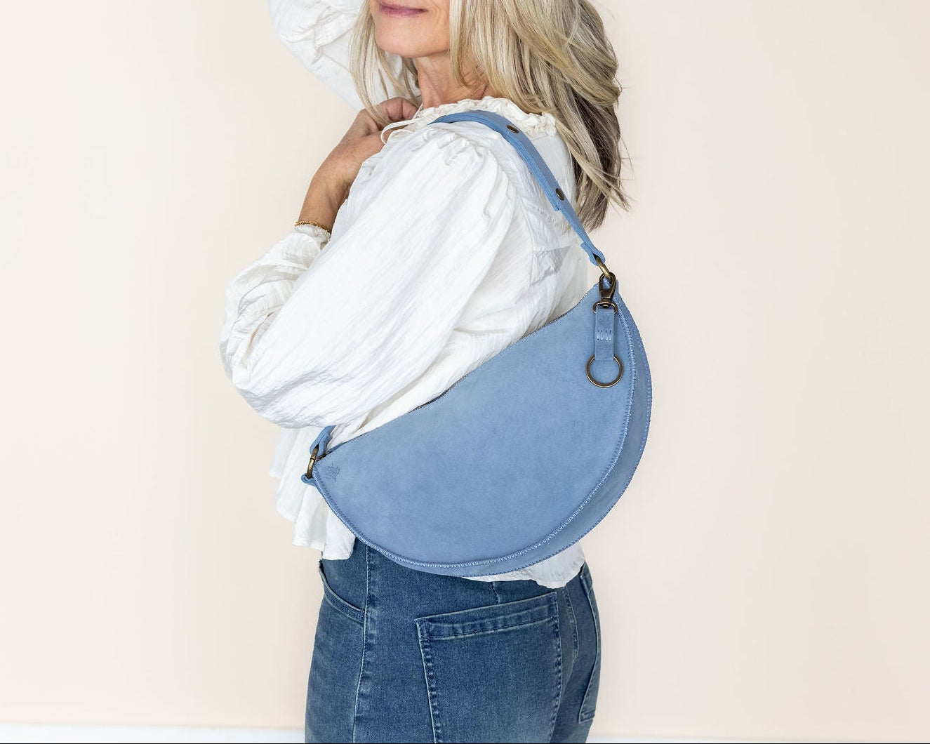 Woman wearing a blue denim bag over her shoulder against a plain background