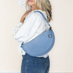 Woman wearing a blue denim bag over her shoulder against a plain background