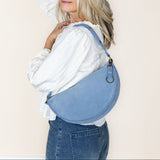 Woman wearing a blue denim bag over her shoulder against a plain background