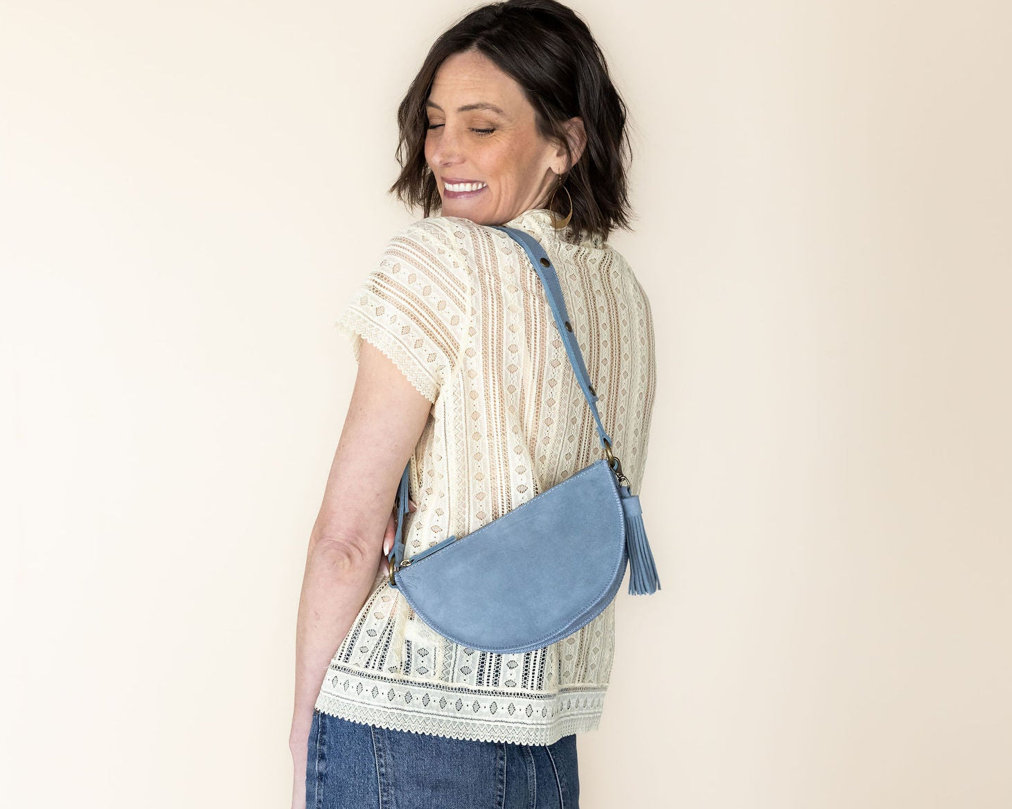 Woman carrying a blue crossbody bag against a beige background