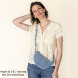 Woman wearing a beige blouse and blue jeans with an extended strap over her shoulder on a white background