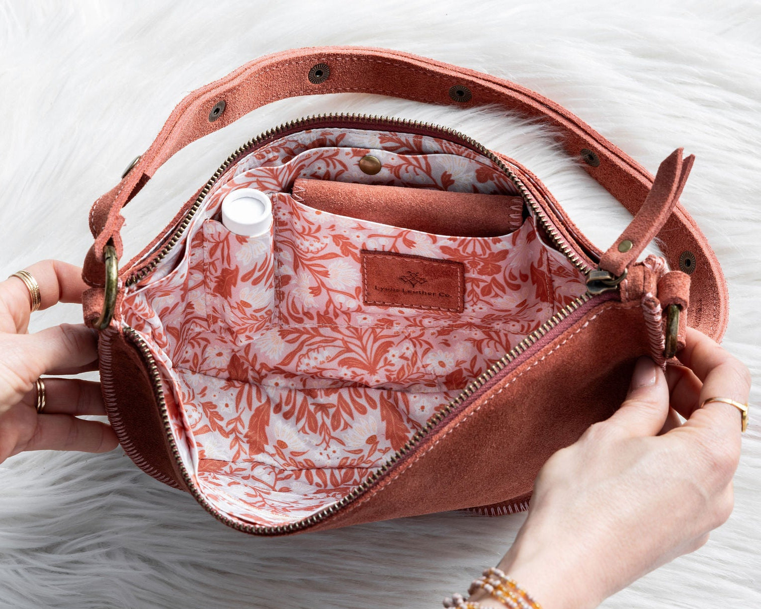 Person opening a pink handbag with floral interior on a white surface