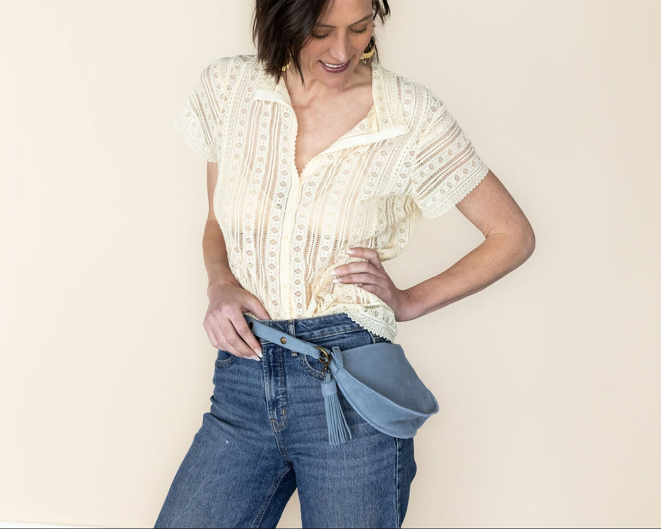 Woman wearing a white lace top and blue jeans against a plain background