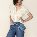 Woman wearing a white lace top and blue jeans against a plain background