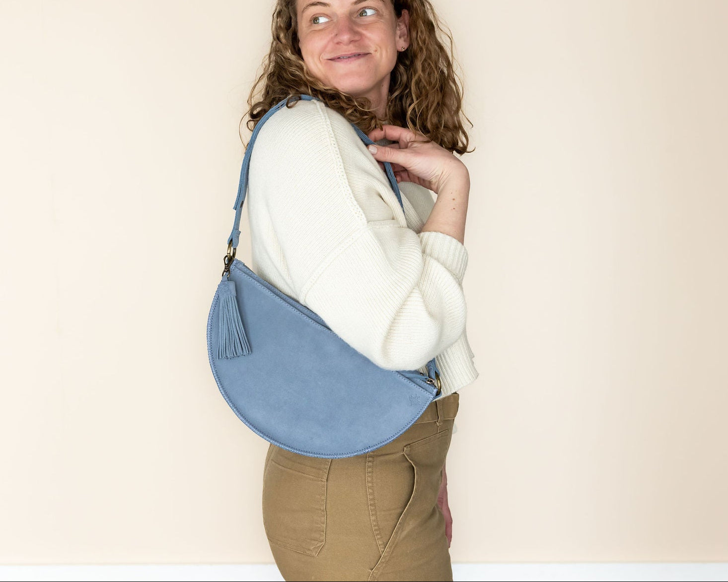 Woman holding a blue sling bag against a plain background