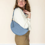 Woman holding a blue sling bag against a plain background
