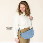 Woman holding a blue crossbody bag with an extended strap against a beige background