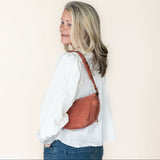 Woman wearing a white shirt and blue jeans with a mauve leather bag on a beige background