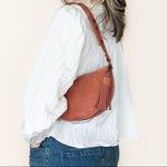 Woman wearing a white shirt and blue jeans with a brown leather bag on a beige background