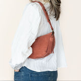 Woman wearing a white shirt and blue jeans with a brown leather bag on a beige background