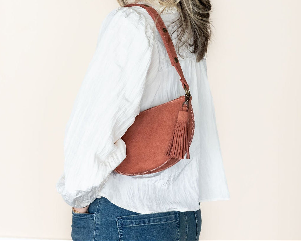 Woman wearing a white shirt and blue jeans with a brown leather bag on a beige background