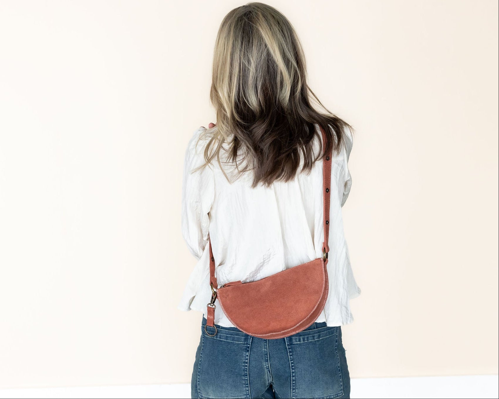 Person wearing a mauve crossbody bag on a plain background
