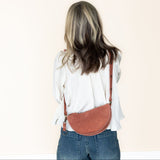 Person wearing a mauve crossbody bag on a plain background