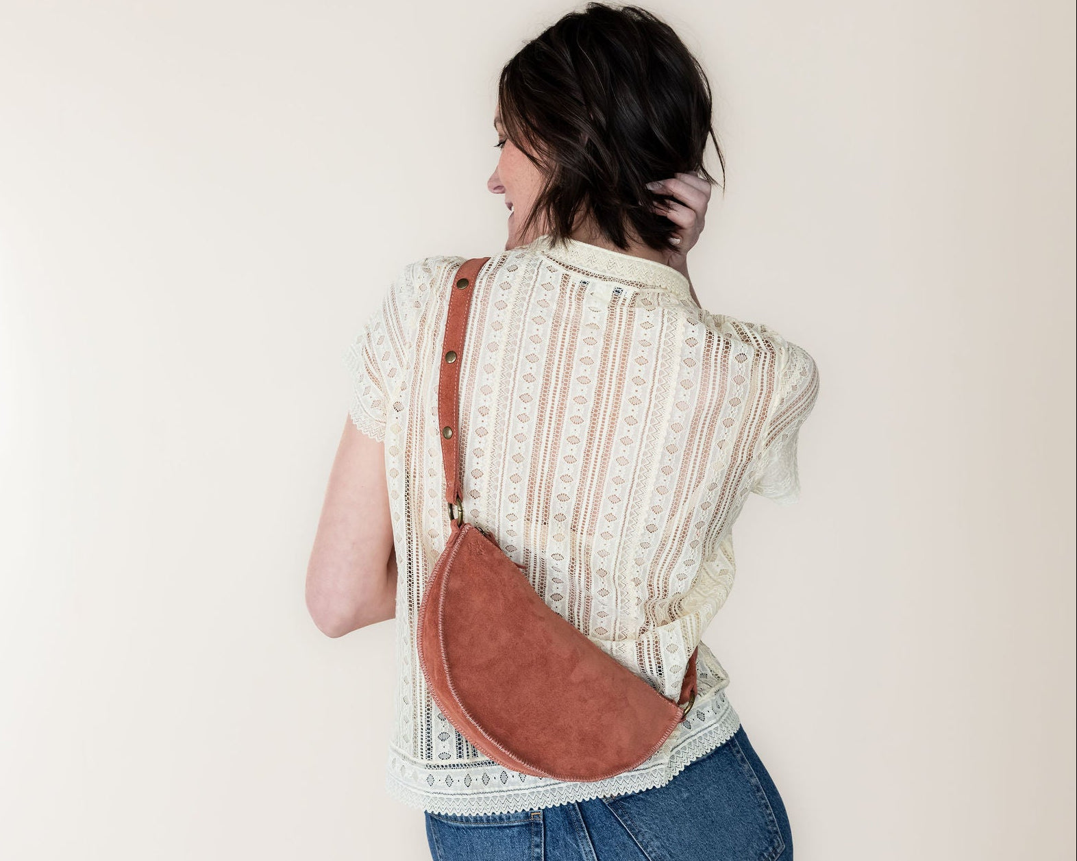 Person wearing a patterned shirt and jeans with a mauve crossbody bag against a plain background