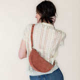 Person wearing a patterned shirt and jeans with a mauve crossbody bag against a plain background