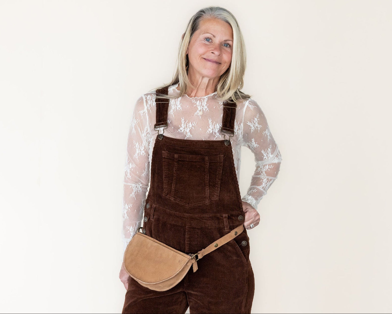 Woman wearing brown overalls with a beige bag on a white background