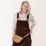 Woman wearing brown overalls with a beige bag on a white background