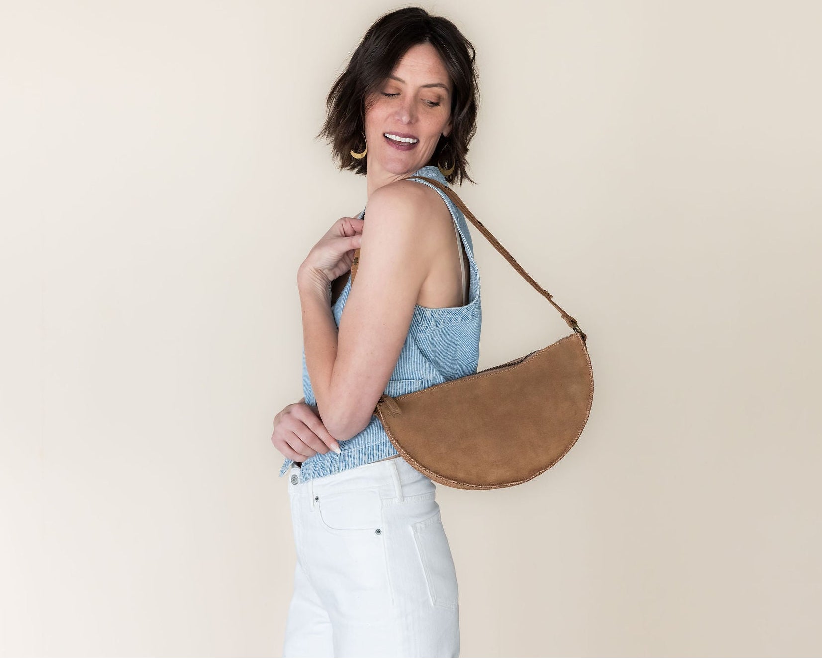 Woman holding a brown leather handbag against a plain background