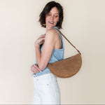 Woman holding a brown leather handbag against a plain background