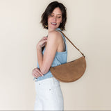Woman holding a brown leather handbag against a plain background