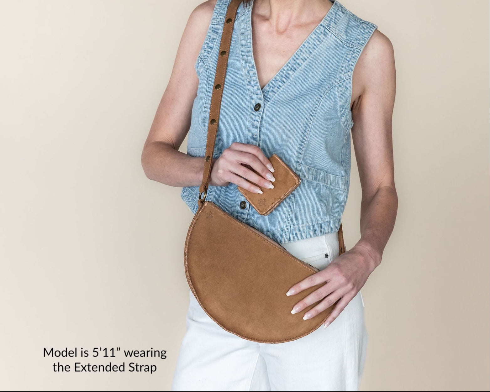 Woman wearing a denim vest and holding a brown leather bag against a beige background