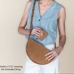 Woman wearing a denim vest and holding a brown leather bag against a beige background
