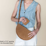 Woman wearing a denim vest and holding a brown leather bag against a beige background