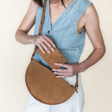 Woman holding a brown leather bag against a plain background