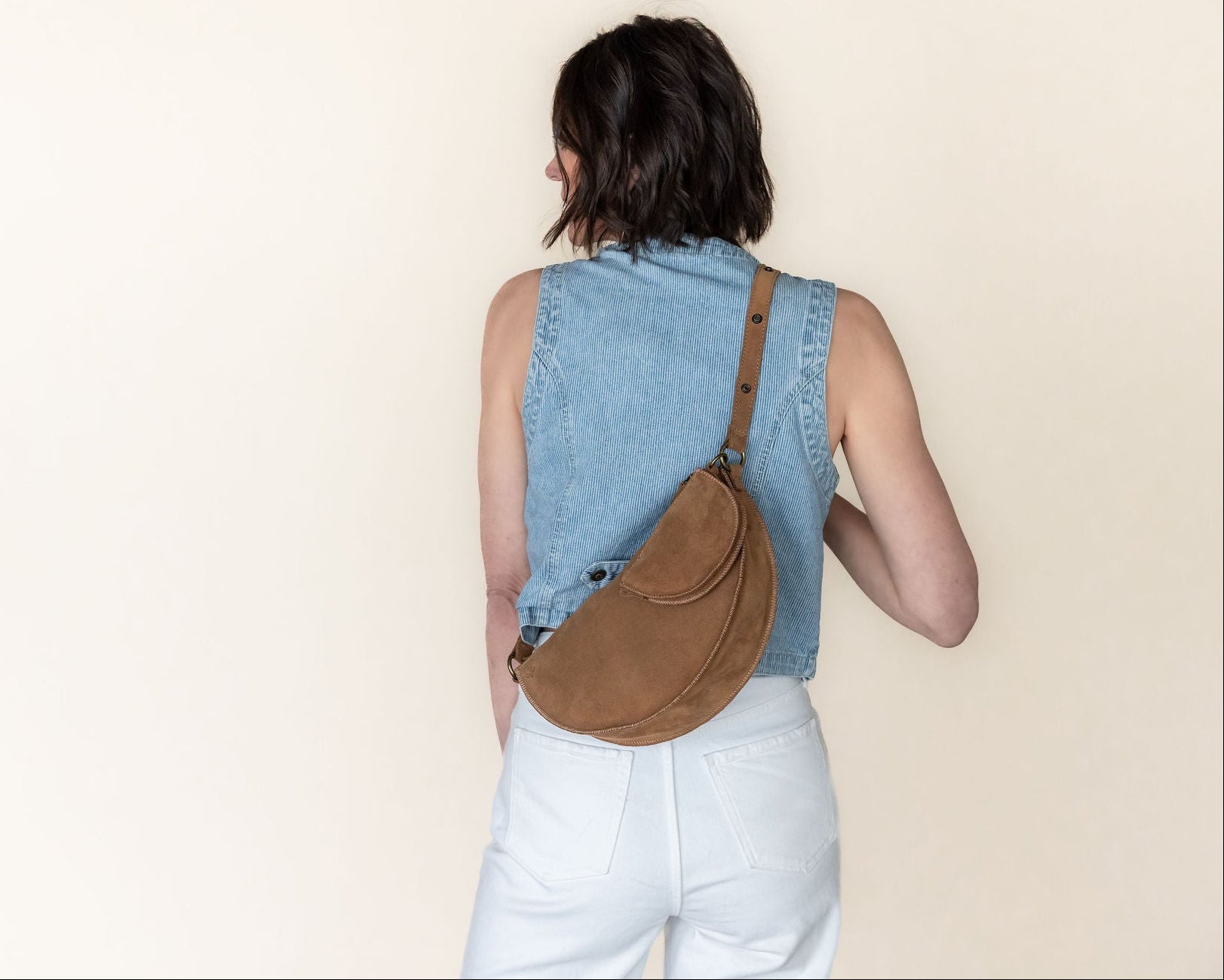 Person wearing a denim vest and carrying a brown bag on a beige background
