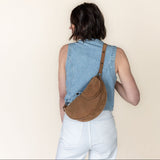 Person wearing a denim vest and carrying a brown bag on a beige background