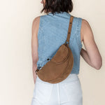 Person wearing a denim vest and carrying a brown bag on a beige background