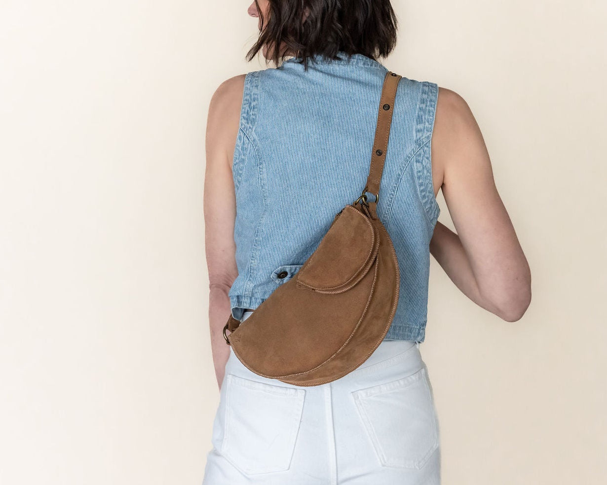 Person wearing a denim vest and carrying a brown bag on a beige background