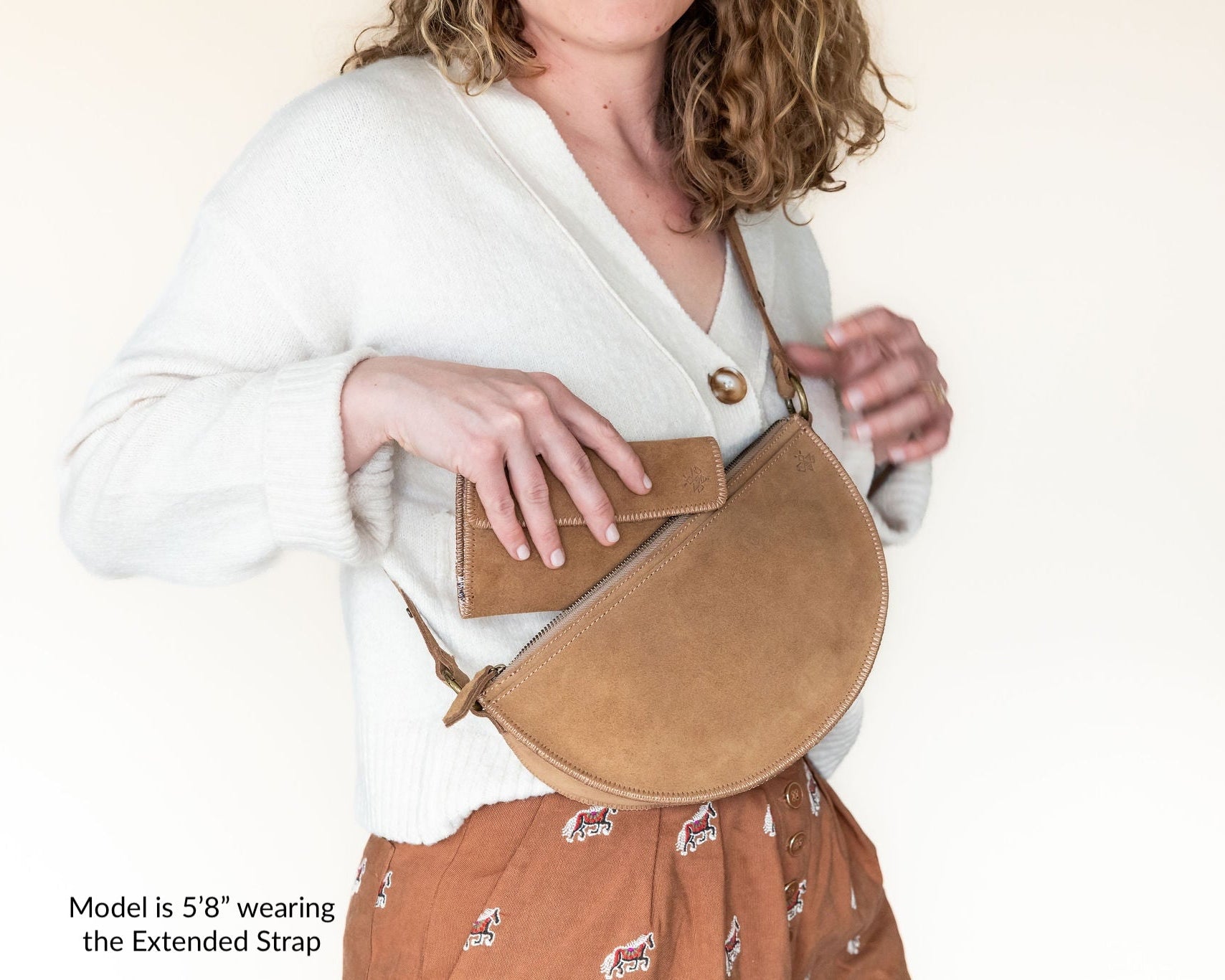 Woman wearing a beige crossbody bag with an extended strap on a plain background