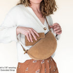 Woman wearing a beige crossbody bag with an extended strap on a plain background