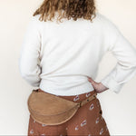 Person wearing a white sweater and brown skirt with a tan belt bag on a plain background