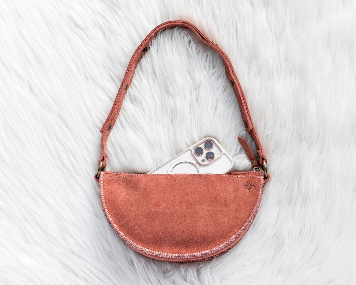 Mauve leather bag with a phone inside on a white fur surface